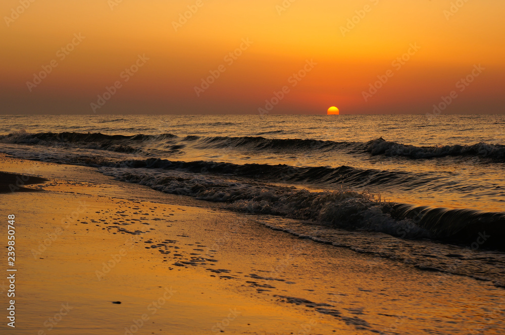 Sunrise with a beautiful orange sun rising from the Black Sea waves. Empty beach landscape.