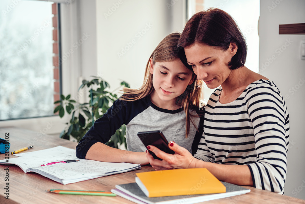 Mother using smart phone and helping daughter with homework Mother using smart phone and helping daughter with homework