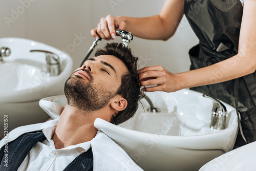 cropped shot of professional hairstylist washing hair to male client in beauty salon