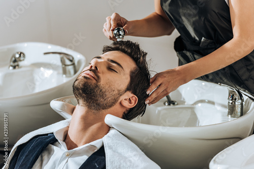 Fotografie cropped shot of young hairdresser washing hair to handsome client in beauty salo