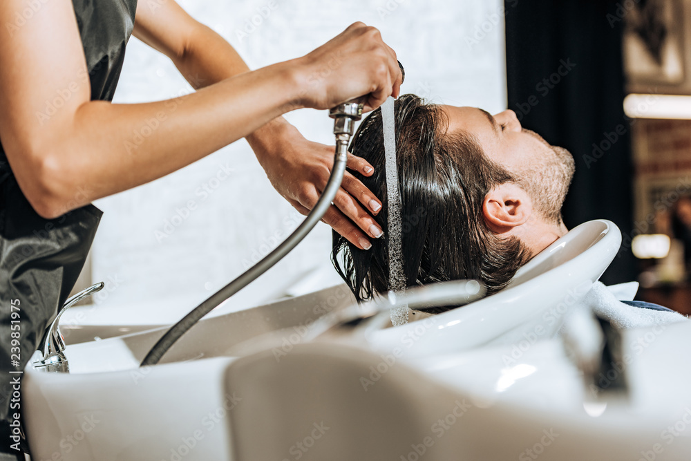 partial view of hairdresser washing hair to handsome young man in beauty salon partial view of hairdresser washing hair to handsome young man in beauty salon