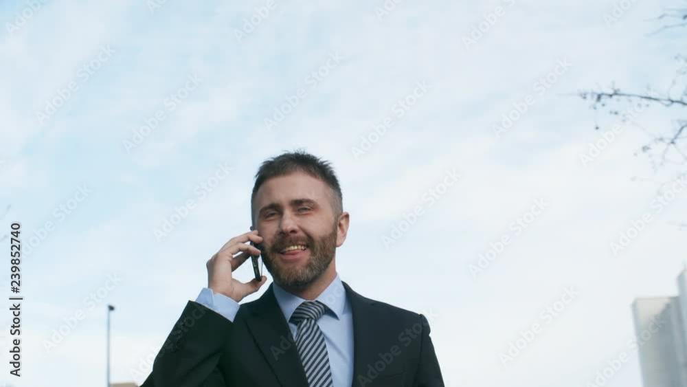 Pan shot of Caucasian businessman talking on phone outdoors Pan shot of Caucasian businessman talking on phone outdoors