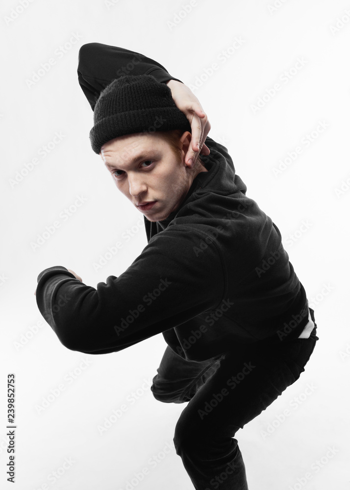 Young freestyle dancer dressed in black jeans, sweatshirt, hat and gray sneakers is dancing in the studio on the white background Young freestyle dancer dressed in black jeans, sweatshirt, hat and gray sneakers is dancing in the studio on the white background