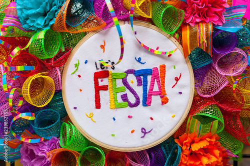 The word `fiesta` stitched in colorful letters on multicolored mash decorated with ribbons, glitter and paper flowers. Decoration for Fiesta Festival.