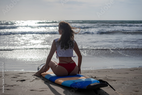 Beach lifestyle people - woman enjoying summer sun and blue sky sitting relaxing with surfboard after bodyboarding in water. Beautiful multiracial Asian Caucasian female bikini girl on travel vacation