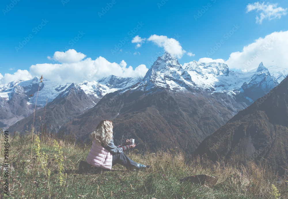 woman traveler drinks coffee with a view of the mountain landscape. A young tourist woman drinks a hot drink from a cup and enjoys the scenery in the mountains. Trekking concept.