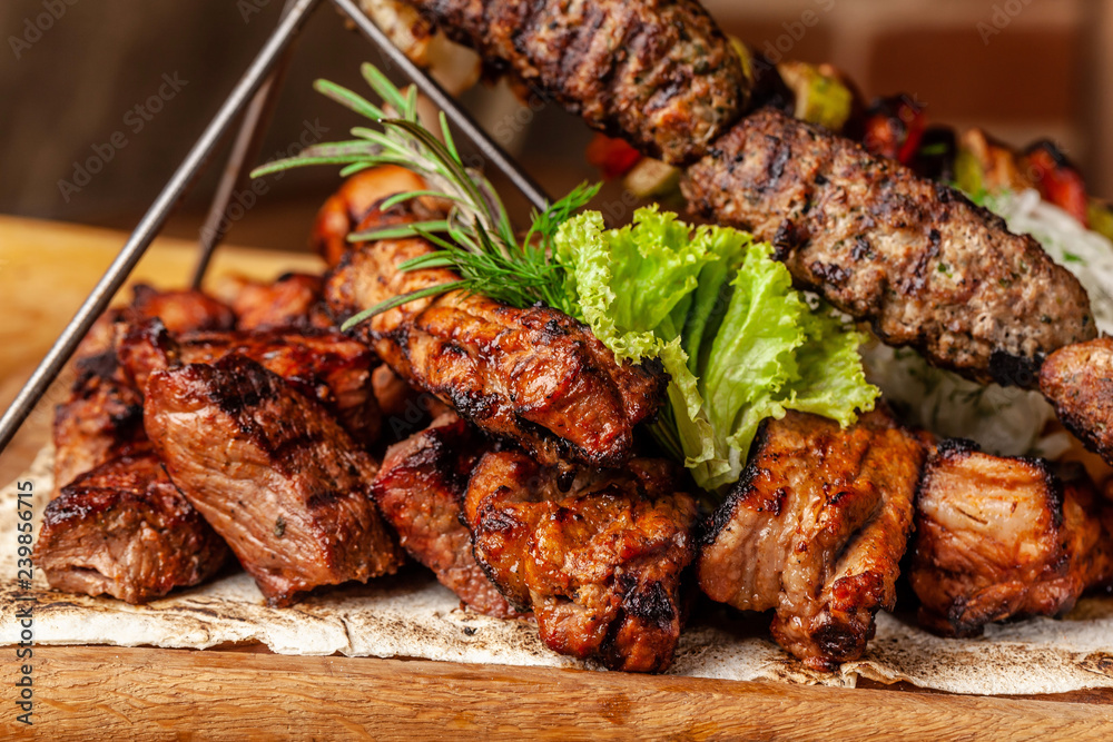 The concept of Georgian cuisine. Meat board with shashlik, grilled pork ribs, lulya kebab and shish kebab. Grilled french fries and grilled vegetables. Meat feed on a wooden board.