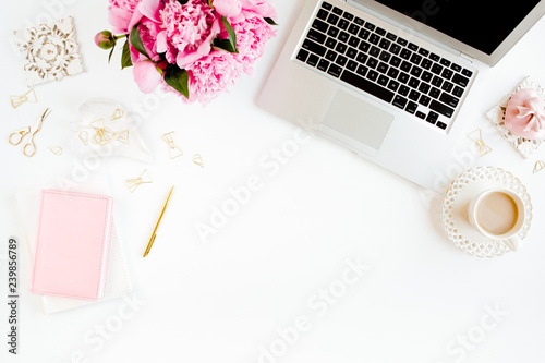 Flat lay women's office desk. Female workspace with laptop, pink peonies bouquet, accessories on white background. Top view feminine background.