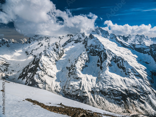Mountain peaks covered with snow. Sunny day in the snowy mountains. Clouds above the mountain tops. Beautiful mountain background
