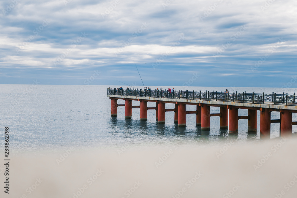 Sea pier. Fishermen fishing on the pier. Sea and clouds above