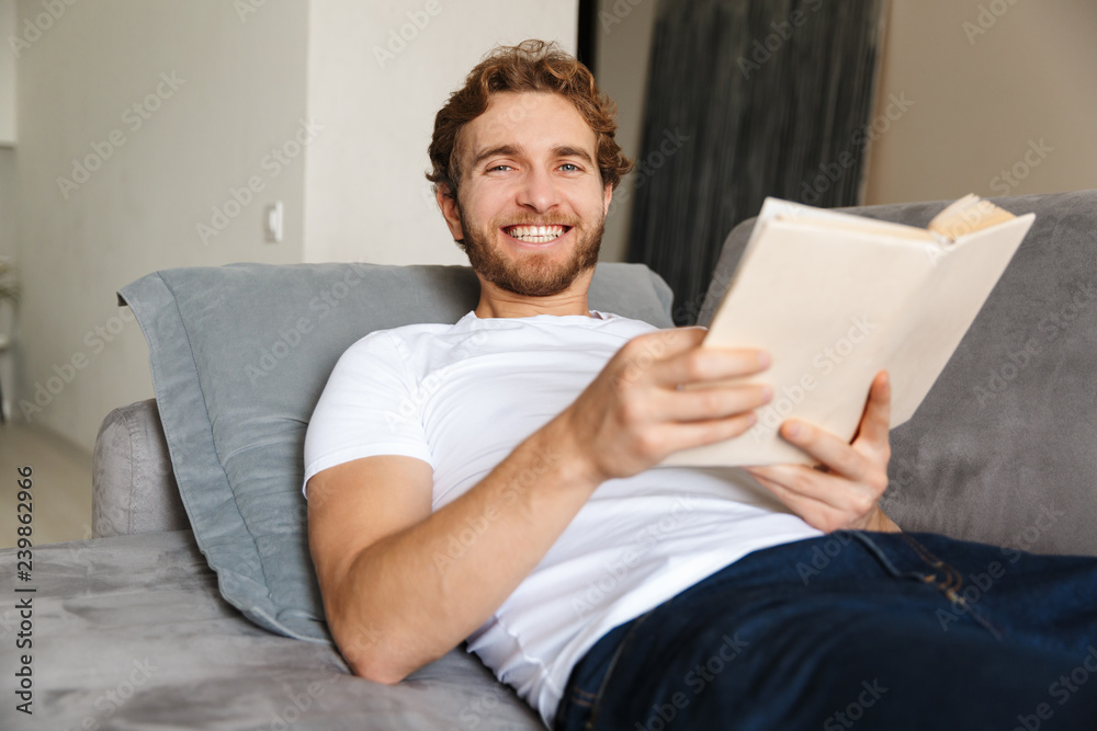 Handsome young bearded man on sofa at home reading book. Handsome young bearded man on sofa at home reading book.