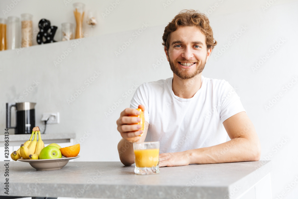 Happy young bearded man at the table at home make a juice with fruits.
