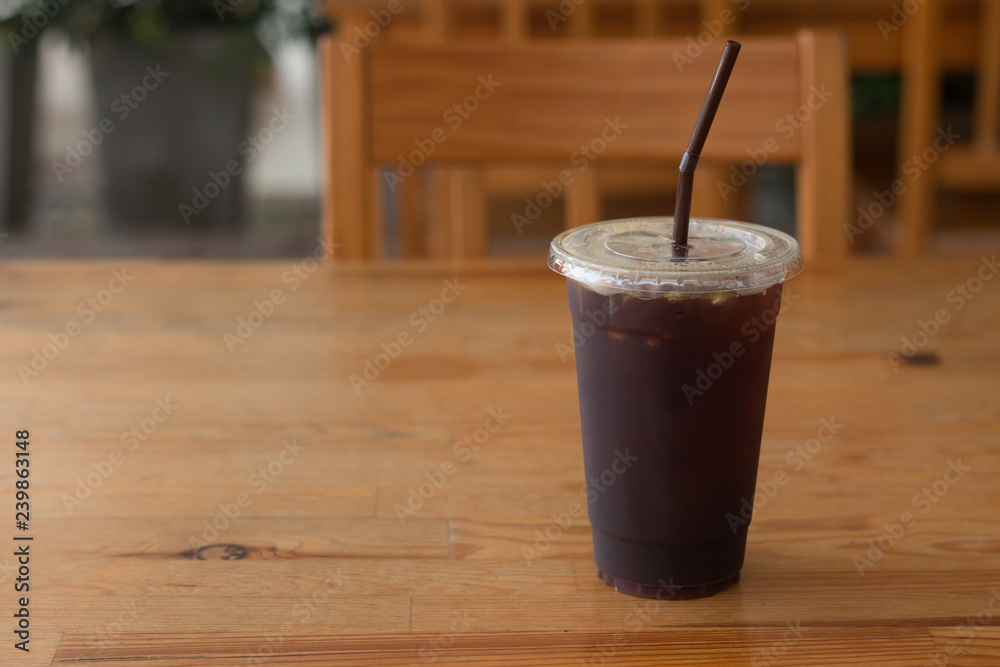 Americano iced coffee in takeaway plastic cup on wooden desk in coffee's shop Americano iced coffee in takeaway plastic cup on wooden desk in coffee's shop