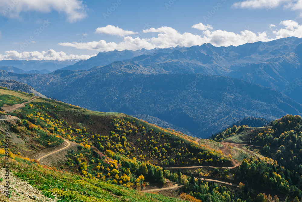 The slopes of the mountains are covered with autumn forest shrubs and herbs. Colorful autumn landscape. Warm autumn Sunny day. Clouds over the mountains