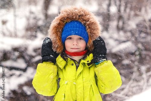 Cute little boy walking under the snow. Happy smiling boy in winter clothes. Snowy winter weather. Beautiful winter park. Kid having fun outdoors. First snow. Christmas holidays. Happy childhood.