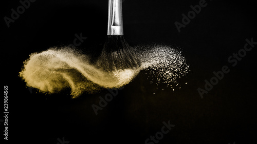 Cosmetic brush with golden cosmetic powder spreading for makeup artist or beauty blogger in black background, look like a luxury