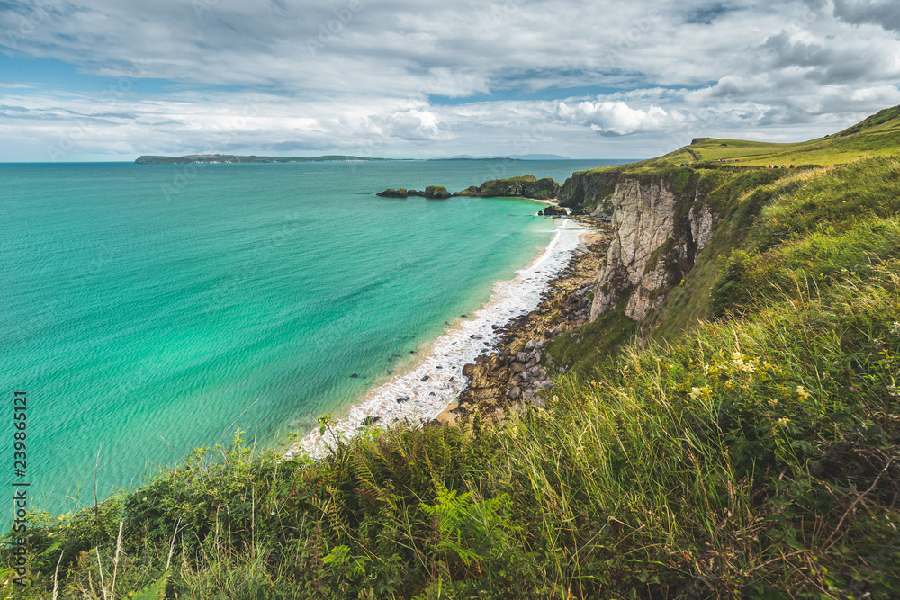 Northern Ireland shoreline. Crystal clear water surface next to the picturesque grass covered land. Stunning Irish landscape. White sand beach as an ideal place for the rest and relax.