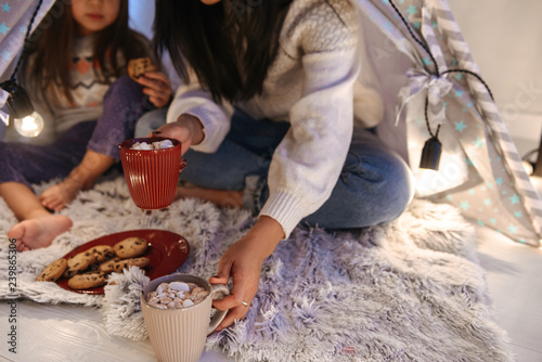 Photo of beautiful asian family mother and daughter eating cookies, while sitting together at home in children playing tent