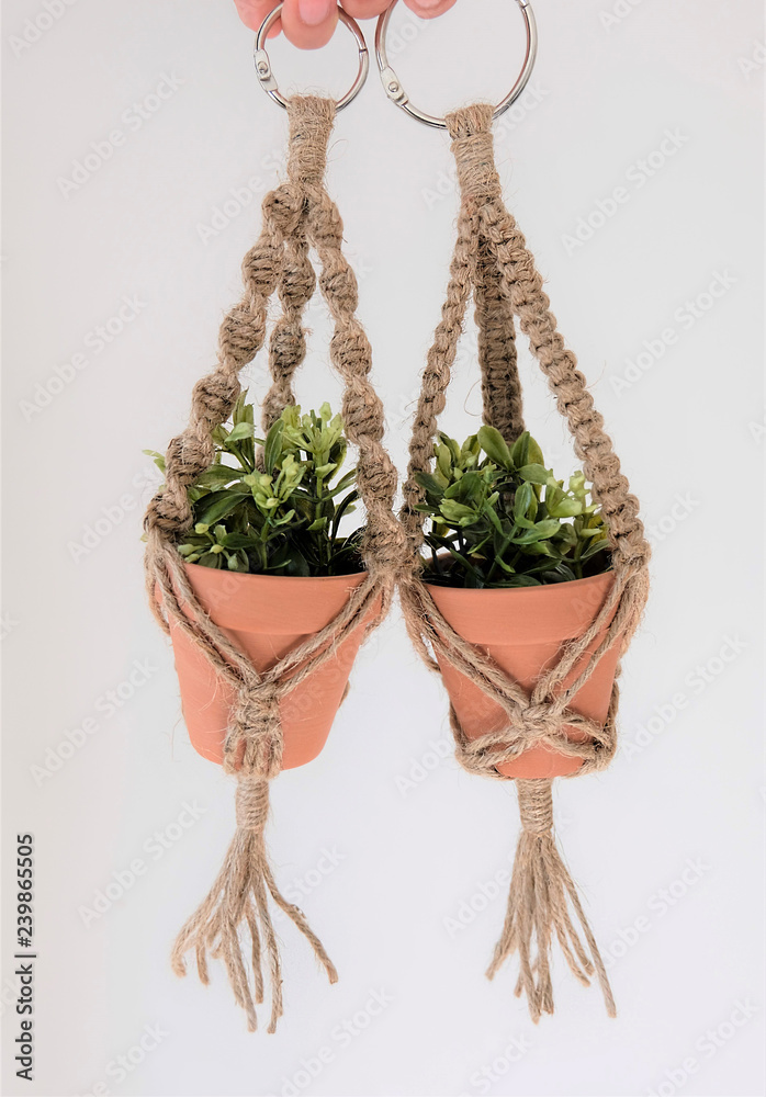 Two mini macrame plant hangers made out of 100% jute twine are being held up by hands. Fake plants are in the ceramic pots.