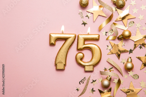 Number 75 gold celebration candle on star and glitter background photo