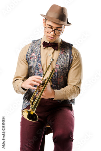 young male jazzman holding trumpet and sitting on chair isolated on white