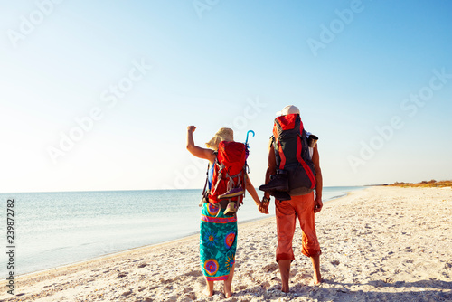 Couple of travelers with backpacks stands on a deserted beach