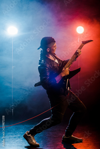 young male musician playing on electric guitar on stage with smoke and dramatic lighting