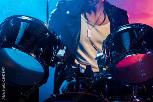 cropped shot of male musician playing drums during rock concert on stage with smoke and dramatic lighting