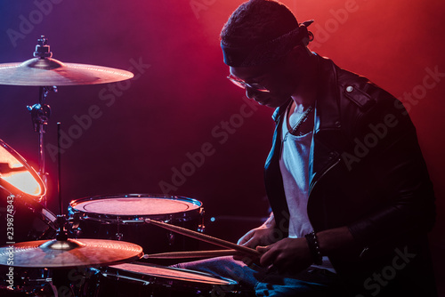 mixed race male musician in leather jacket playing drums during rock concert on stage