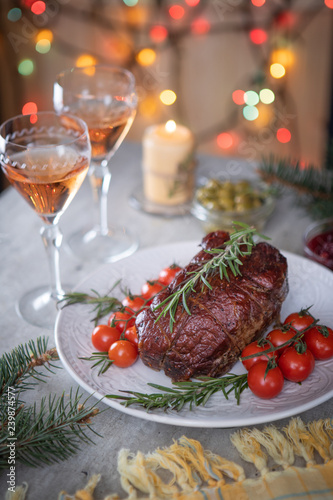 Roast beef and confit tomatoes on the holiday table on the background of Christmas lights