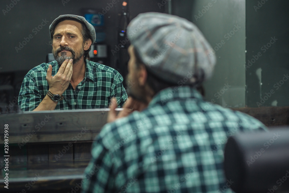 Careful man touching his beard while being in barber shop Careful man touching his beard while being in barber shop