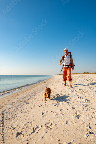 Joyful traveler with funny dog goes along the deserted beach