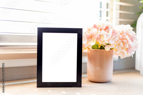Blank black color picture frame template for place image or text inside on the desktop table work space with laptop and flower. window light