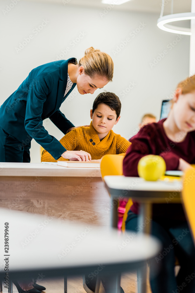 young female teacher helping schoolchildren studying at desks
