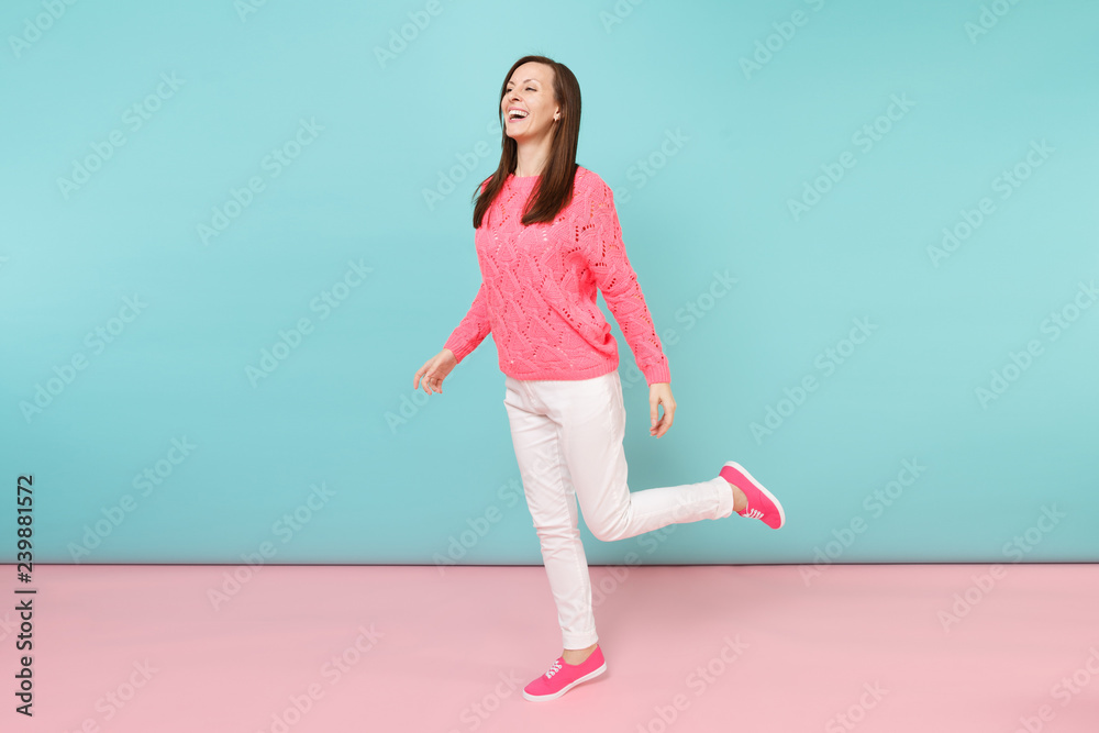 Full length portrait of smiling young woman in knitted rose sweater, white pants posing isolated on bright pink blue pastel wall background in studio. Fashion lifestyle concept. Mock up copy space.