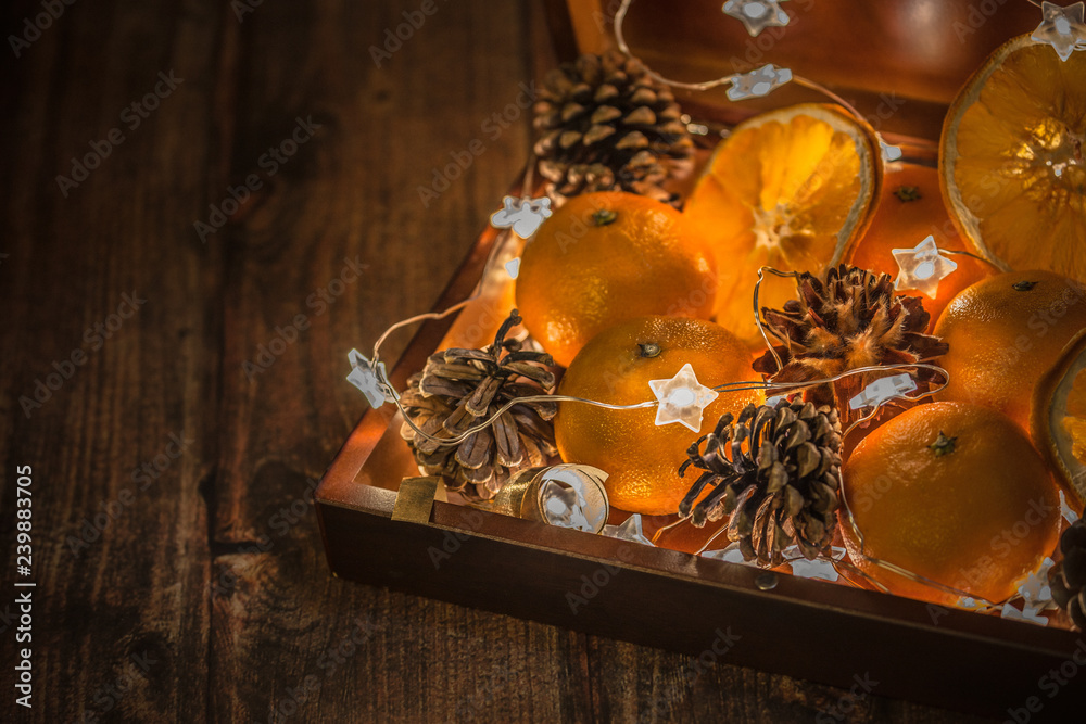 orange mandarins in wooden box with light garland and cones, present for christmas and new year, stars lights