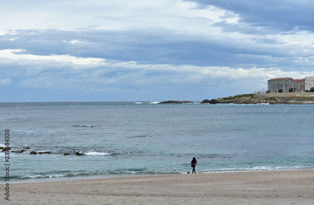 Riazor beach with woman walking a dog. Rainy day, La Coruna, Spain.