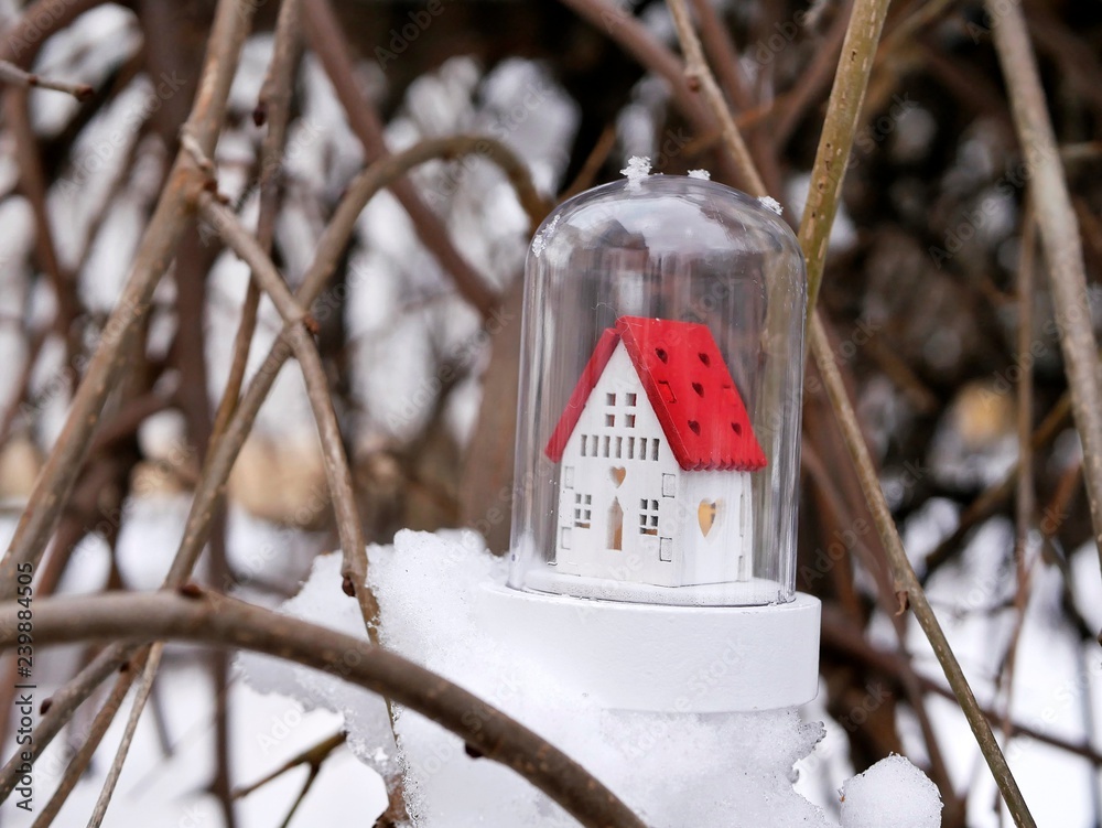 Naklejka premium Small toy decorative white house with a red roof and lighted illumination on a snow-covered tree, the concept of winter seasonal holidays, Christmas, a new home in the new year, home comfort