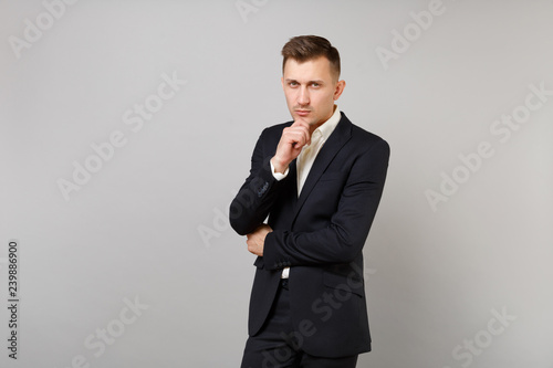 Portrait of confident young business man in classic black suit and shirt put hand prop up on chin isolated on grey background in studio. Achievement career wealth business concept. Mock up copy space.