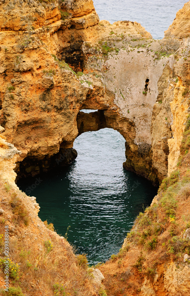 Ocean water seen through hole in rocks. Stone arches, caves, rock formations at Dona Ana Beach (Lagos, Algarve coast, Portugal) in the evening light.