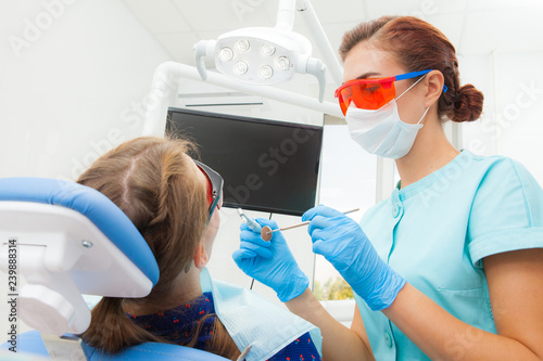 Young woman - orthodontist dentist treats patient's teeth lying in the dental chair in the dental clinic. Patient young woman