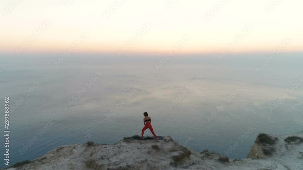 Beautiful woman is stretcing on the top of mountain with sea view at sunset. Aerial footage. Back view. Beautiful woman is stretcing on the top of mountain with sea view at sunset. Aerial footage. Back view.