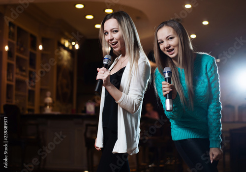 Beautiful women singing karaoke songs in microphones in restaurant