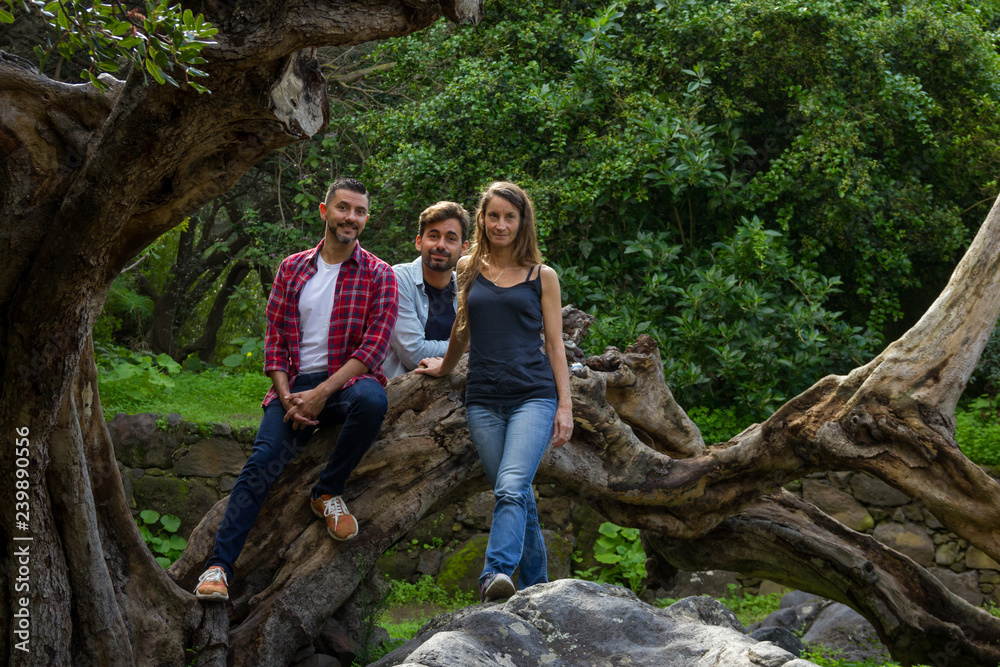 Naklejka premium Beautiful young people standing on fabulous tree trunk in botanical garden of Gran Canaria, Spain. Group of tourists enjoying day trip in forest