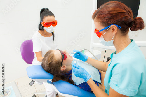 A young woman is a dentist orthodontist and a female assistant treats a patient s teeth lying in a dental chair at a dental clinic. A young woman patient