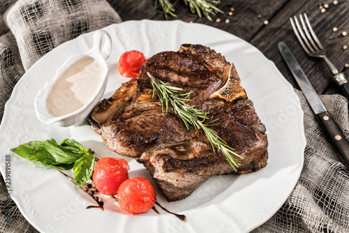 Grilled pork chop steak with rosemary, tomatoes and spices on plate over wooden rustic background. Hot Meat Dishes. Top view, flat lay