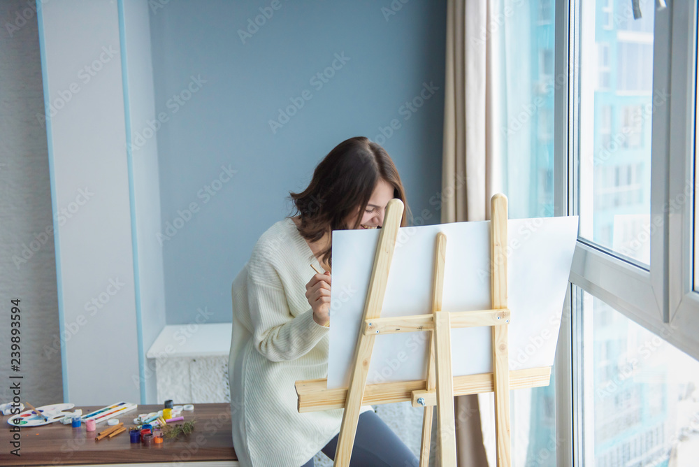 young pretty girl paints a picture in front of a large window young pretty girl paints a picture in front of a large window