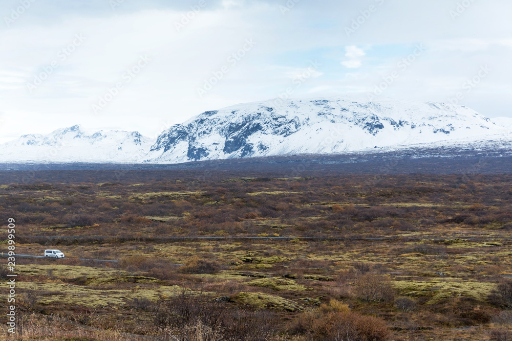 an abandoned landscape in Iceland with a car on the road, in the background of a snowy mountain