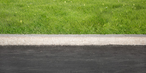 Green Grass Grows Near Black Asphalt, Separated By Concrete Border. Road And Lawn Divided By Concrete Curb.