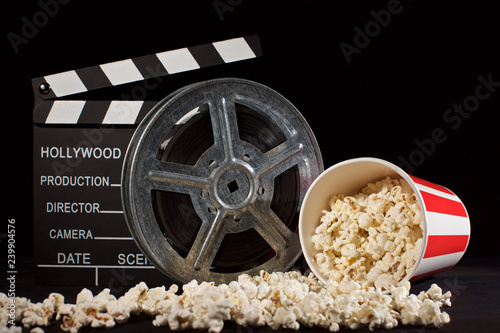 movie film reel and film clapper with popcorn box on black
